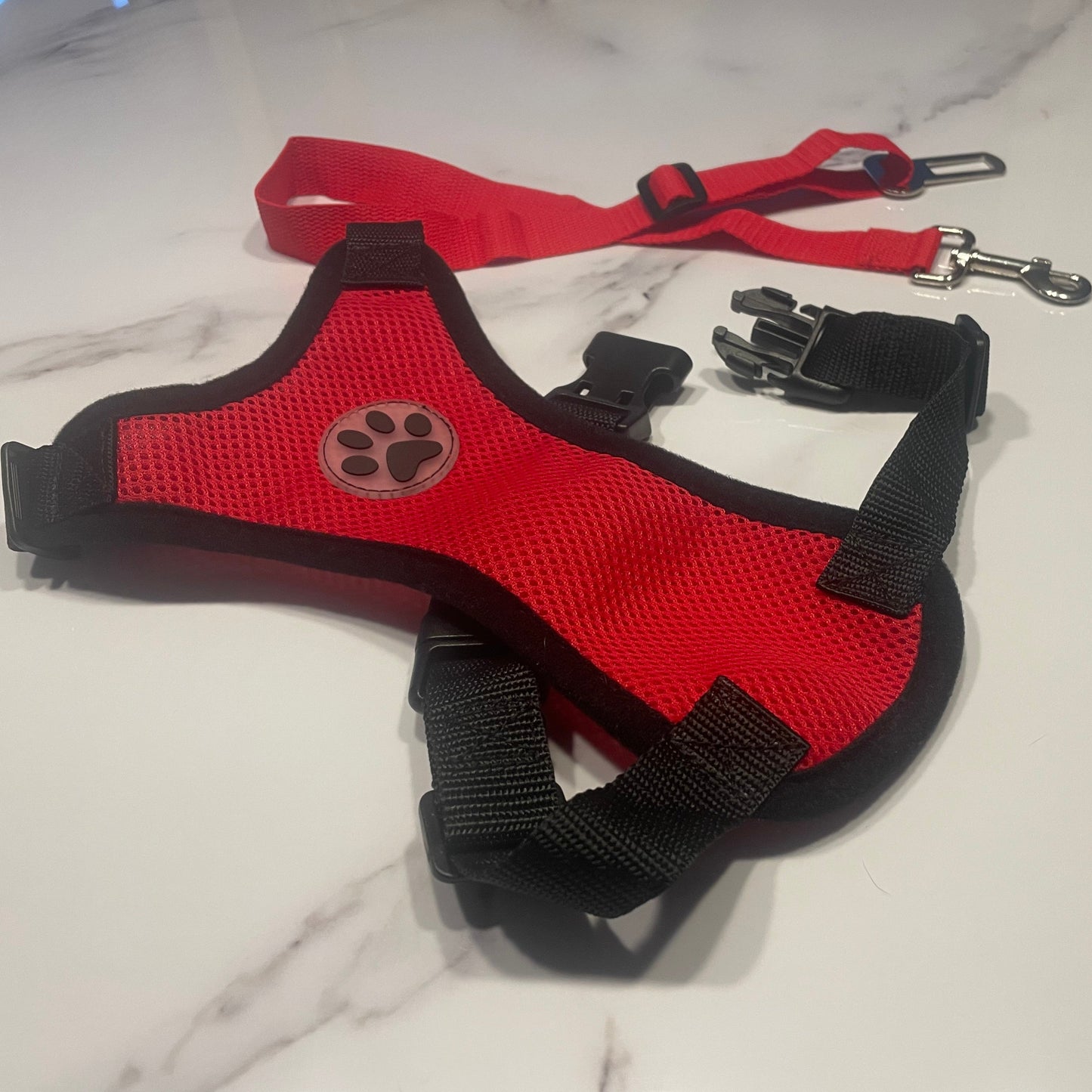 Red and black dog harness with a paw print on a light marble background
