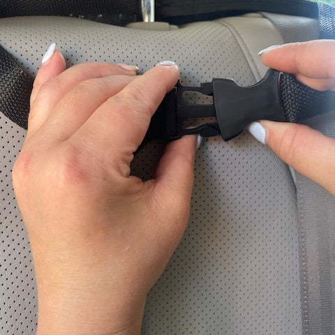 Person adjusting a car seat belt buckle on a car seat.